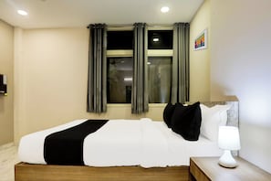 Una habitación de hotel con una cama, una mesita de noche, una lámpara y un ventanal con cortinas.