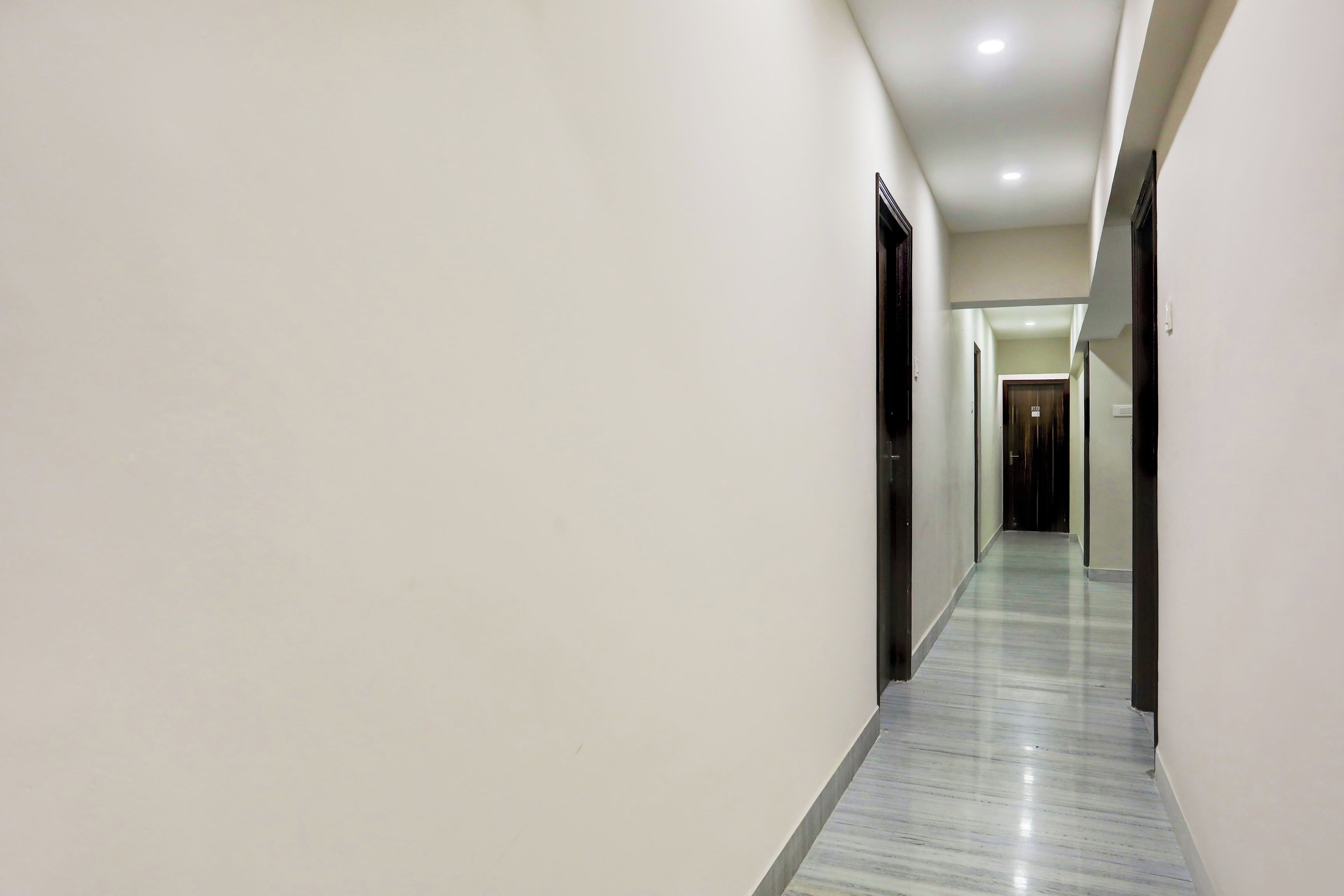 A long, narrow hallway with white walls and a marble floor, leading to a door at the end.