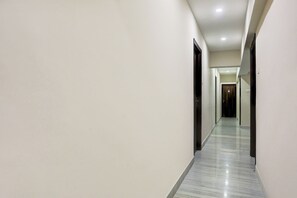 Un largo pasillo estrecho con paredes blancas y suelo de mármol, que lleva a una puerta al final.