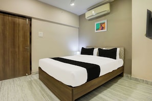 A neatly made bed with a white and black bedspread, a wooden headboard, and a wall-mounted air conditioner. - Hotel O Luxe Villa (Nagpur)