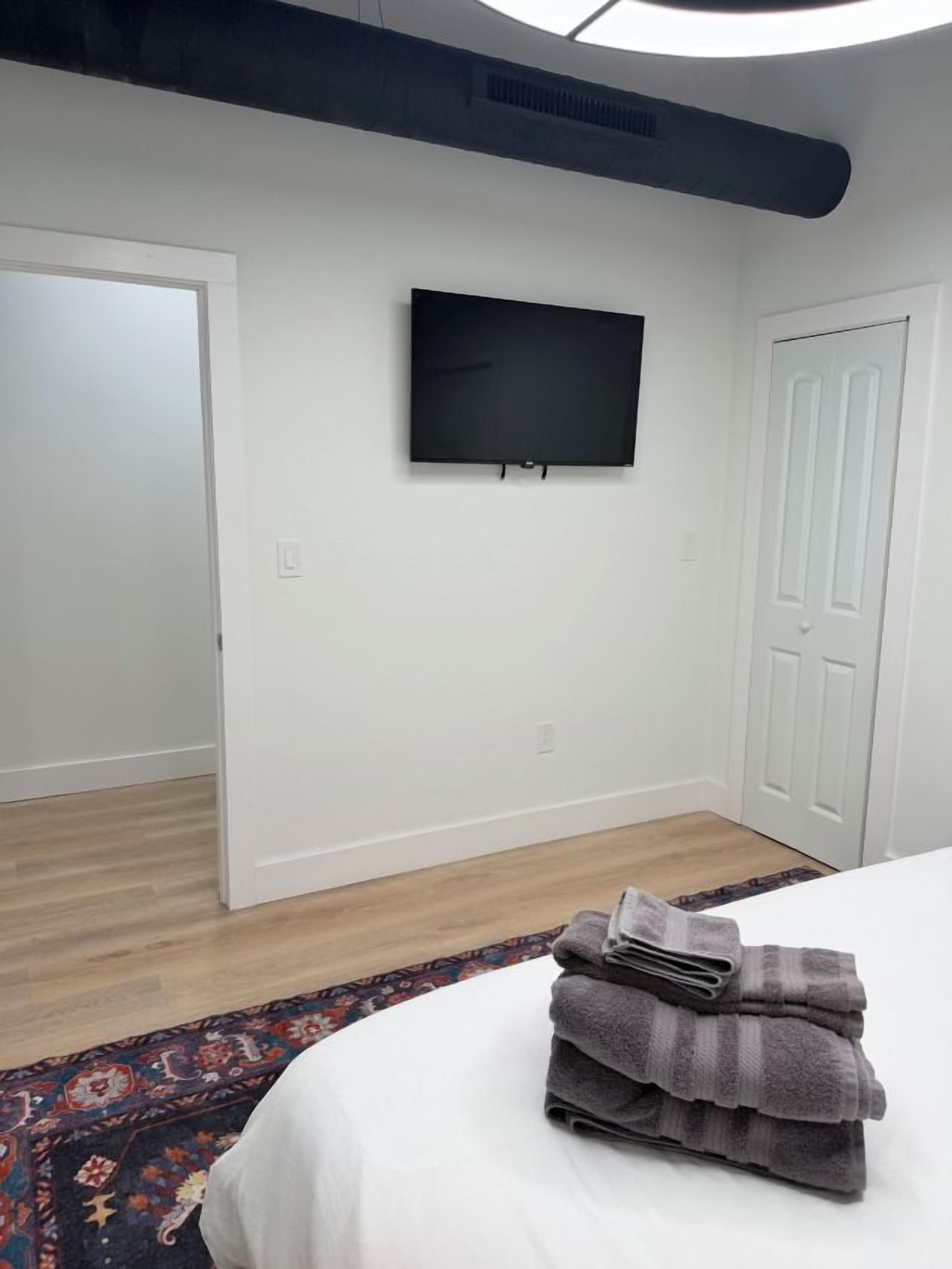 A hotel room with a bed, a flat-screen TV mounted on the wall, and a door leading to another room.