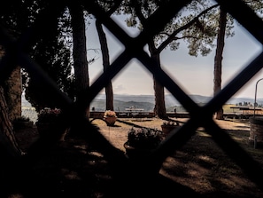Un espace extérieur clos, aménagé avec une table et des chaises, entouré d’arbres et offrant une vue sur des collines lointaines.