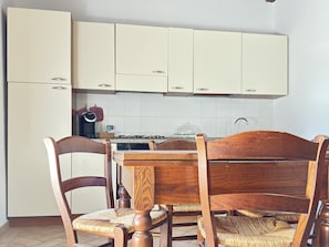 Une cuisine avec des meubles blancs, une table à manger en bois et des chaises avec des assises en osier tressé.