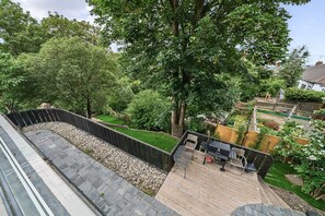 A deck with a stone border, surrounded by lush greenery and a wooden fence. - The Ridge London | Luxury Home (Belvedere)