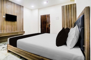 A bedroom with a bed, a television mounted on the wall, and a wooden door.