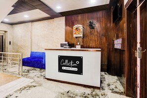 Un área de recepción con suelo de mármol, un sofá azul, un mostrador de madera y un ventilador de pared.