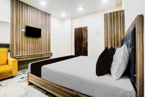 Habitación de hotel con una cama, televisión, pared decorativa de madera, una puerta y un sillón amarillo.