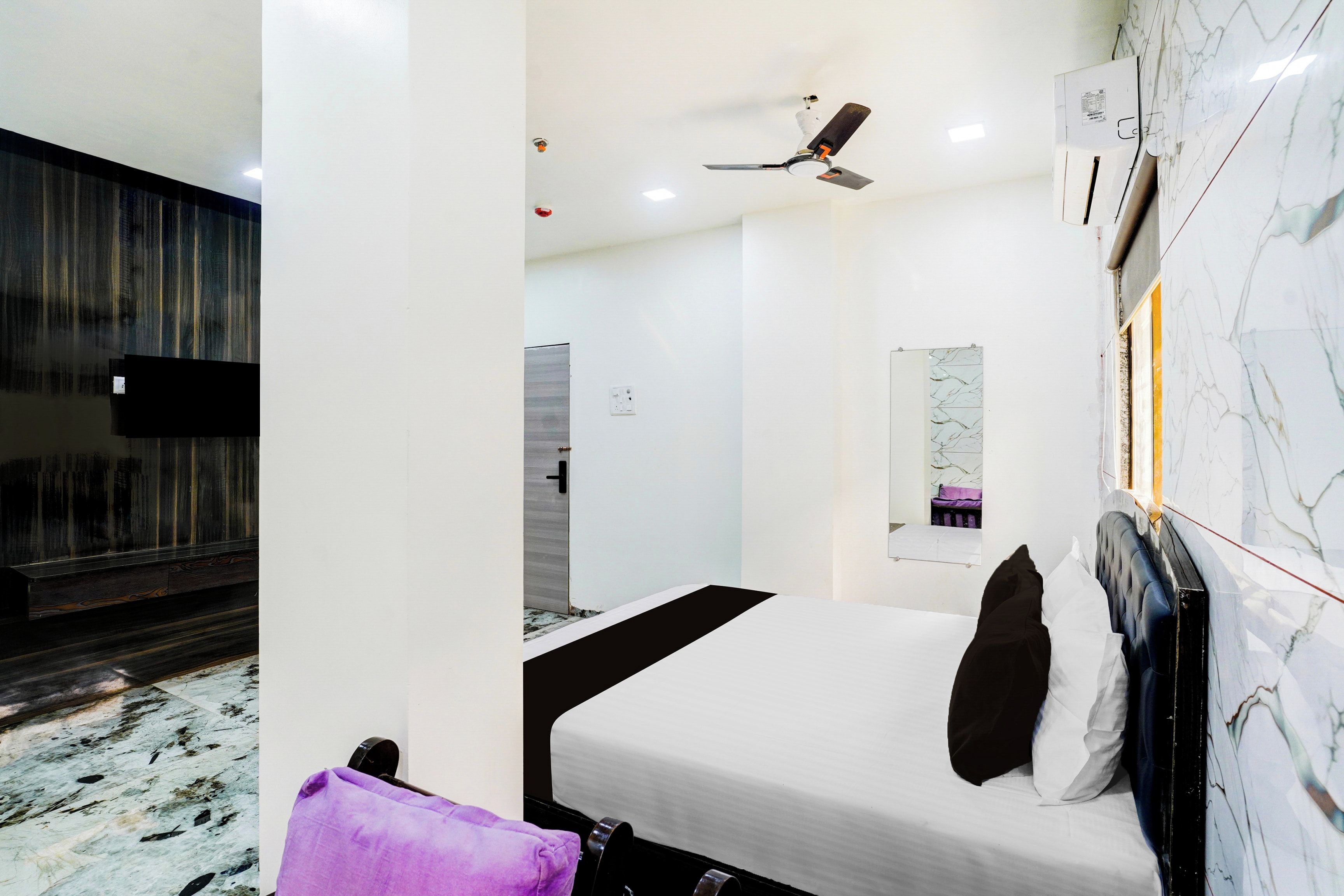 A modern hotel room with a bed, a ceiling fan, a bathroom with a shower, and a marble wall.