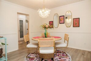 Un comedor con una mesa redonda, cuatro sillas, una araña y espejos en la pared.