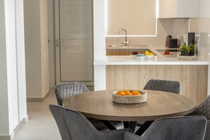 A modern kitchen with a central island, a dining table with chairs, and a basket of oranges on the table. - 3 Bedroom Villa In The Heart of Protaras (Paralimni)