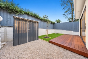 Een achtertuin met een houten terras, een tuinhuis en een stukje gazon.
