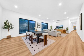 Een moderne woonkamer met een eethoek, grote ramen en een flatscreen televisie.