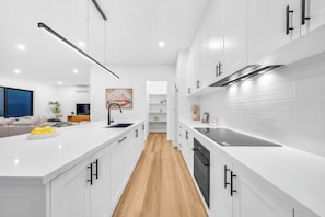 A modern kitchen with white cabinetry, a central island, and a wooden floor. - 2 New Bayswater Homes | 8BR/6BA, Sleeps 16 (Bayswater)