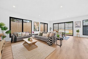A spacious living room with a large sofa, a coffee table, and a dining area with a table and chairs. - 2 New Bayswater Homes | 8BR/6BA, Sleeps 16 (Bayswater)