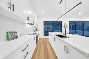 A modern kitchen with white cabinetry, a wooden floor, and a large window with a view of a blue sky and trees. - 2 New Bayswater Homes | 8BR/6BA, Sleeps 16 (Bayswater)