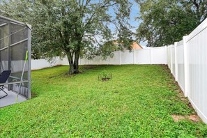 A backyard with a white fence, a tree, and a covered outdoor seating area. - The Cozy Palm Retreat – Heated Pool & Game Room (Davenport)