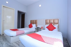 Habitación de hotel con dos camas, cada una con cabecero, mesita de noche y un teléfono, y un almohadón rojo.