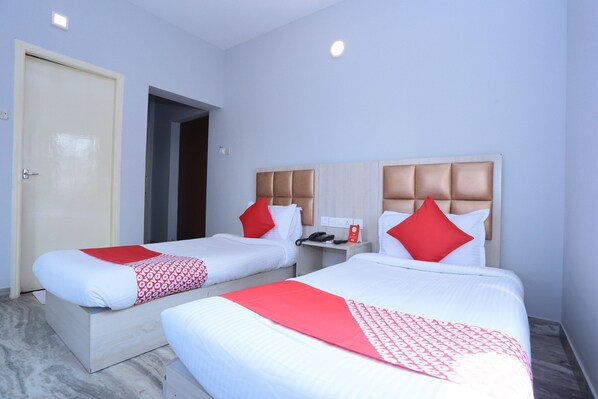 A hotel room with two beds, each with a headboard, a bedside table with a phone, and a red pillow.