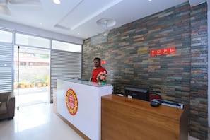 Una recepción de hotel con diseño moderno, un logotipo visible y un cartel que indica servicios como Wi-Fi gratuito, desayuno y cámaras de seguridad disponibles las 24 horas.