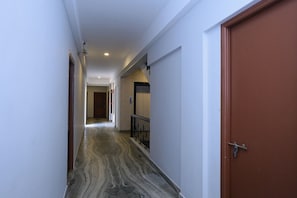 A corridor with a marble floor, a wooden door on the right, and a white wall on the left. - Super Townhouse Prince Palace (Trivandrum)