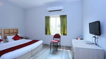 A hotel room with a bed, a desk, a chair, a television, and an air conditioning unit.