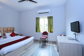 A hotel room with a bed, a desk, a chair, a television, and an air conditioning unit. - Super Townhouse Prince Palace (Thiruvananthapuram)