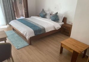 Una habitación de hotel con cama, mesita de noche y un pequeño banco de madera.