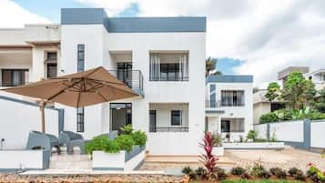 Un edificio residencial moderno de varios pisos, con balcones, mobiliario exterior y un jardín ajardinado.