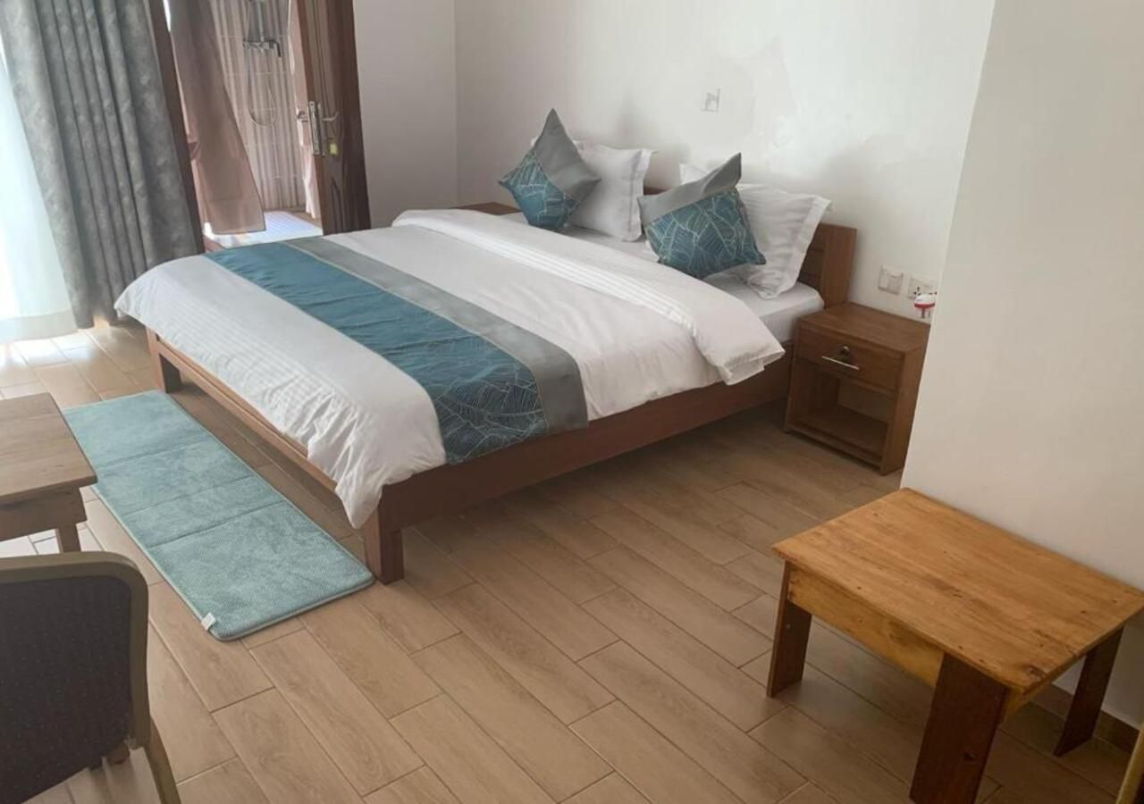 A hotel room with a bed, bedside table, nightstand, and a small wooden bench.