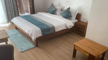 A hotel room with a bed, bedside table, nightstand, and a small wooden bench.