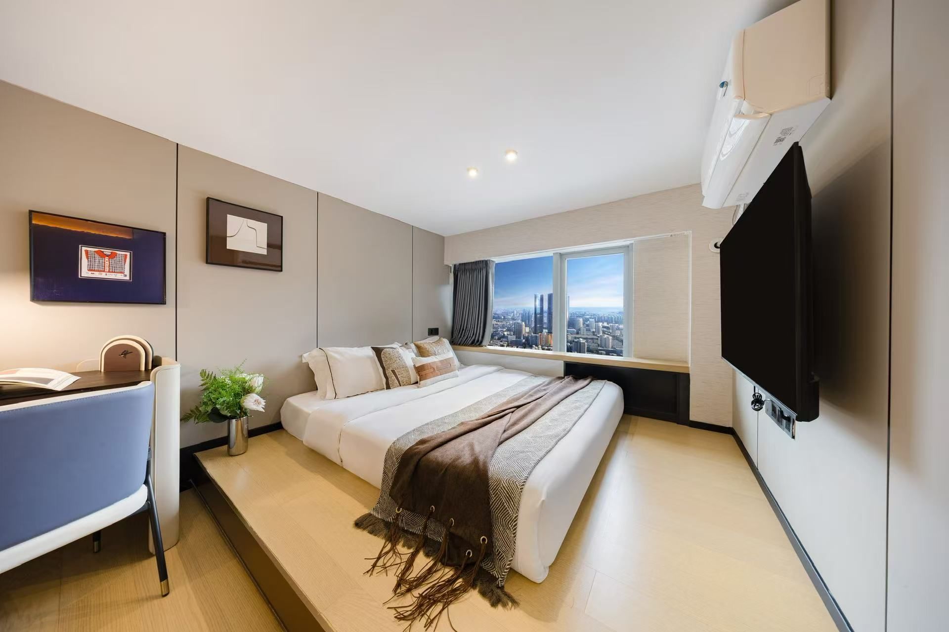 A modern hotel room with a large bed, a desk, a television, and a window with a city view.