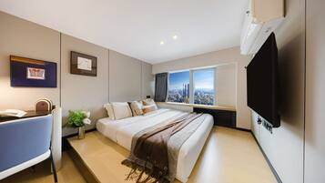 A modern hotel room with a large bed, a desk, a television, and a window with a city view.