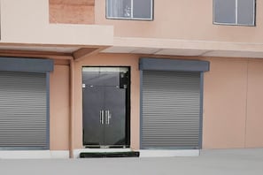 A modern building facade with a central entrance, flanked by two closed roller shutters. - Collection O Radha Krishna Vrindavan (Vrindavan)