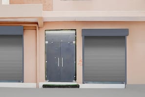 A building facade with a central door and two closed roller shutters. - Collection O Radha Krishna Vrindavan (Vrindavan)