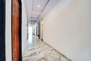 A hallway with a marble floor, white walls, and a wooden door frame. - Collection O Radha Krishna Vrindavan (Vrindavan)