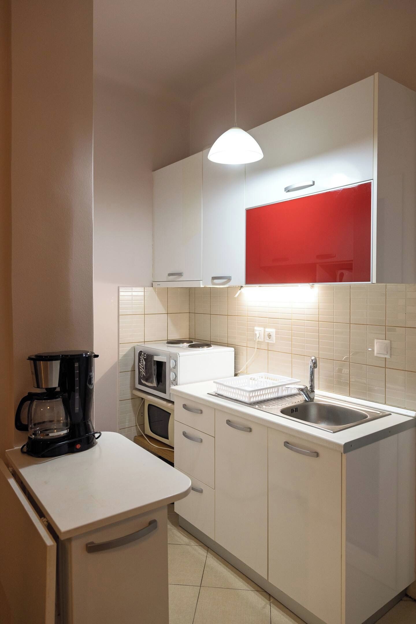 A compact kitchen with a coffee maker, microwave, toaster, and a red-framed mirror above the sink.