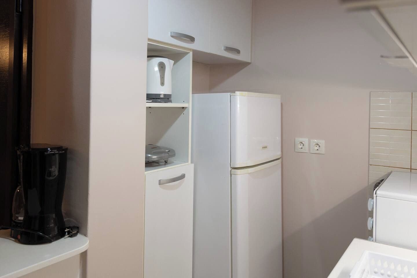 A kitchenette with a white refrigerator, a coffee maker, and a microwave on a white countertop.
