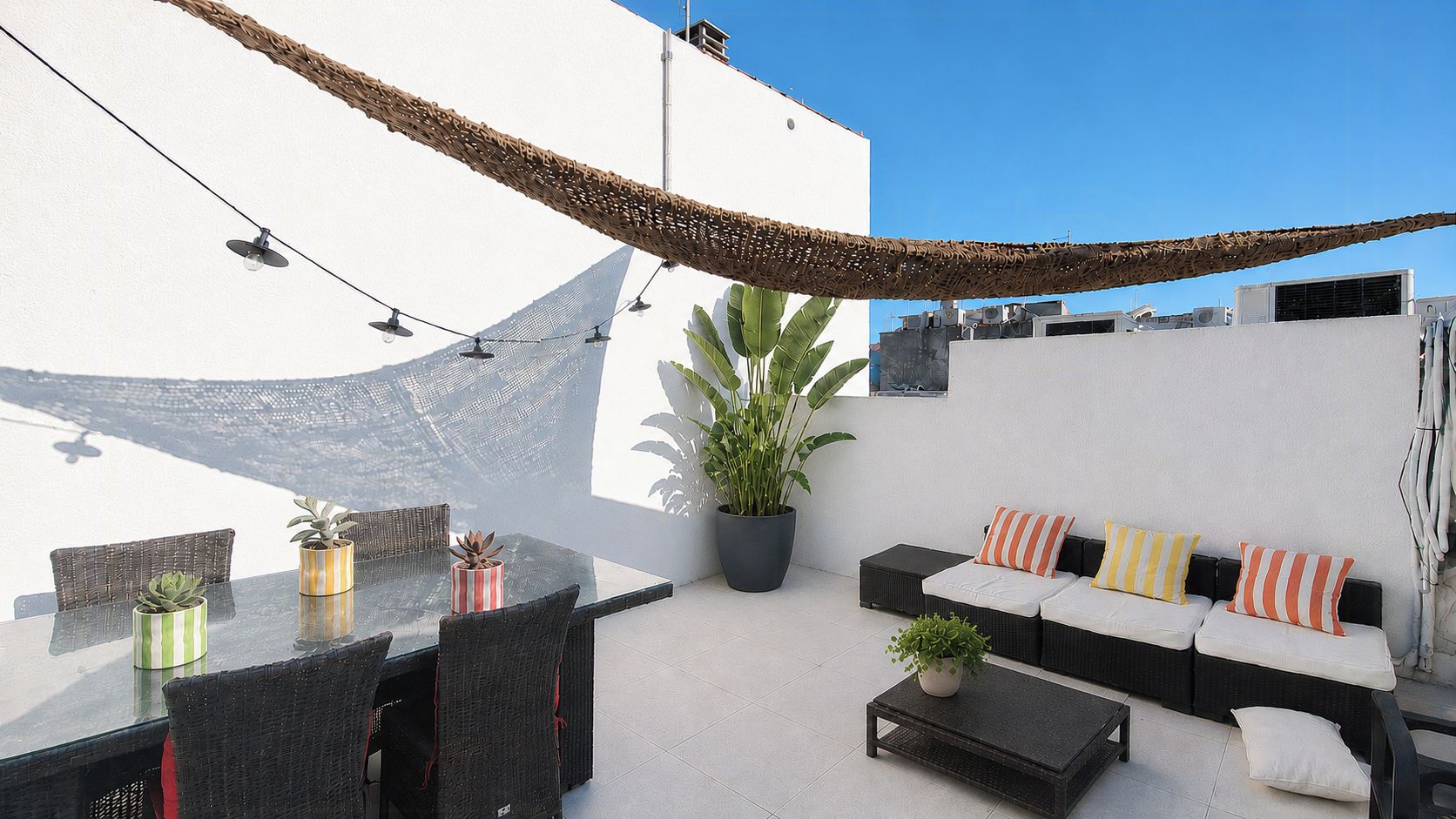 Une terrasse extérieure avec une table à manger, des chaises, un ensemble de canapés et des plantes en pot.