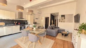 Een moderne keuken met een eethoek, een grijze bank en een aan de muur bevestigde televisie.