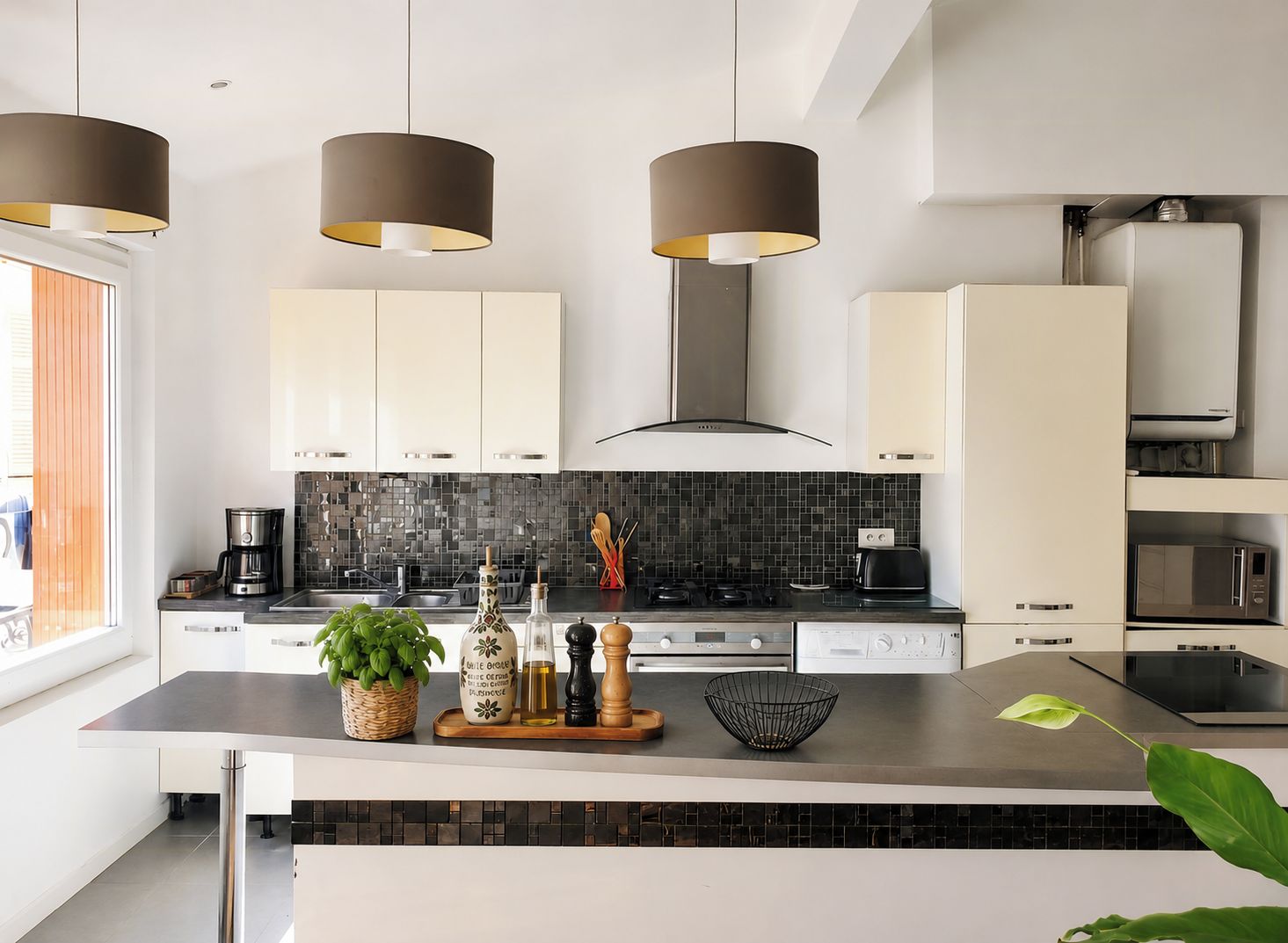 Een moderne keuken met witte kastjes, zwarte aanrechtbladen en een zwart achterwandpaneel. Drie hanglampen, een fornuis en een magnetron zijn aanwezig.