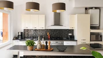 Een moderne keuken met witte kastjes, zwarte aanrechtbladen en een zwart achterwandpaneel. Drie hanglampen, een fornuis en een magnetron zijn aanwezig.