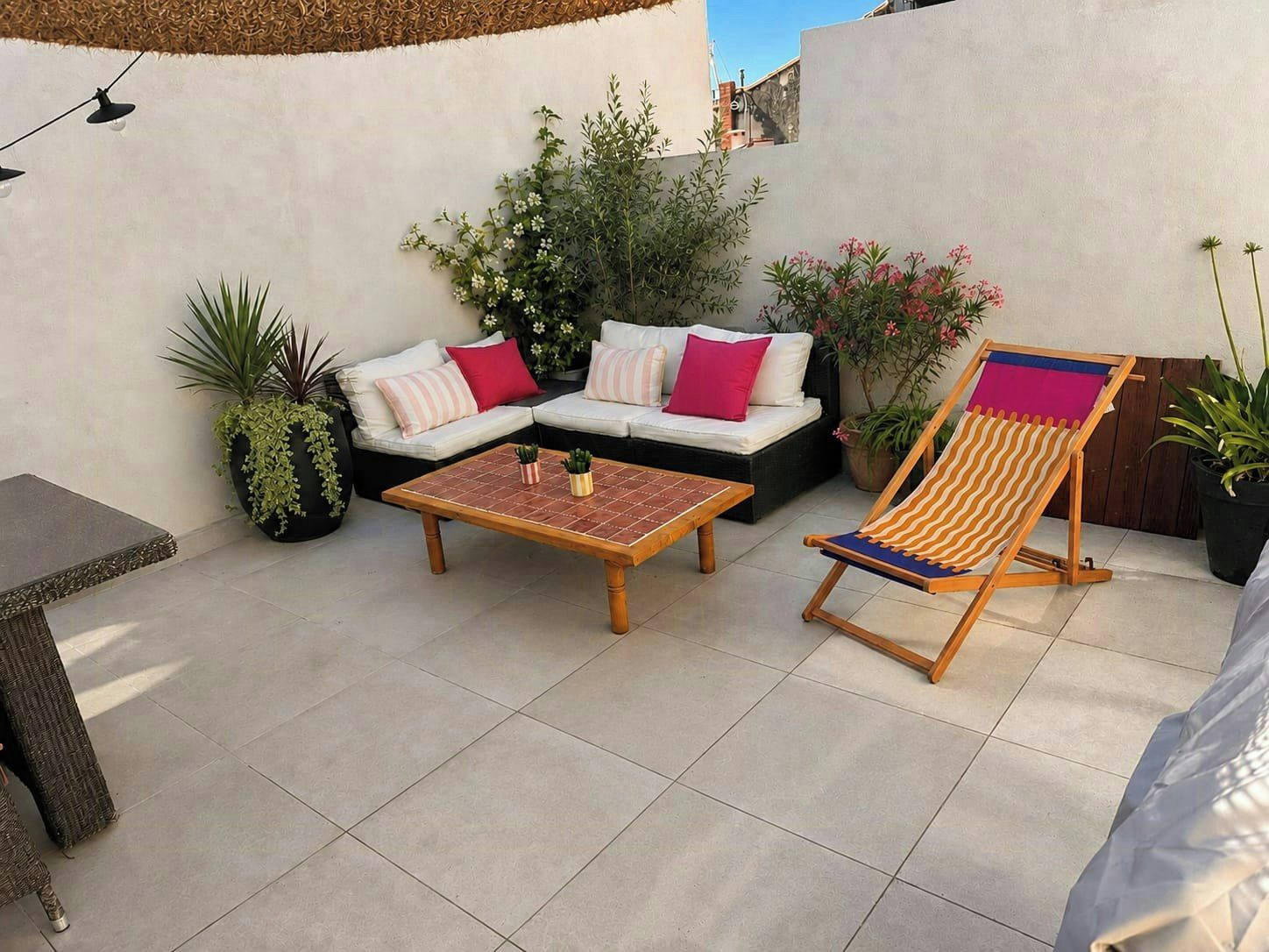 Une terrasse extérieure avec un canapé, une table en bois et un fauteuil de jardin à rayures.