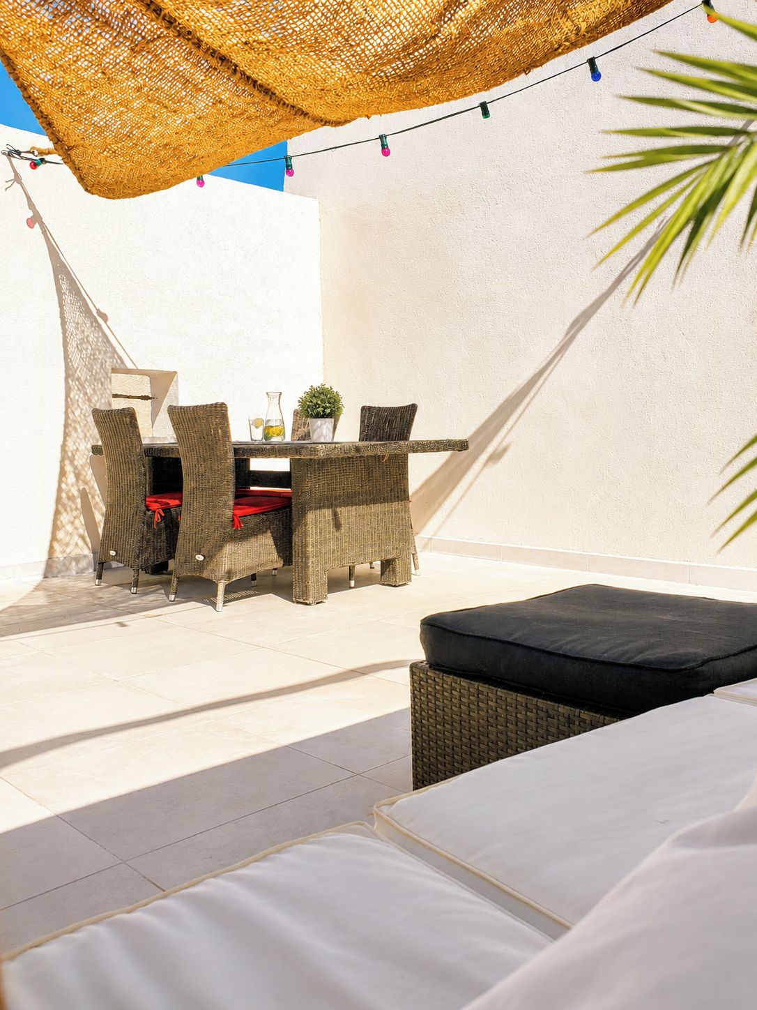 Een terras met rieten meubilair, een tafel met een bloempot en een lichtslingering.