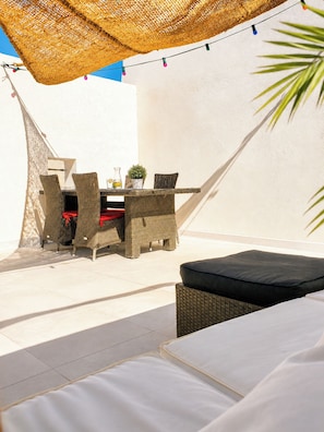 Een terras met rieten meubilair, een tafel met een bloempot en een lichtslingering.