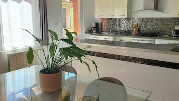 Een moderne keuken met witte kasten, een glazen eettafel en een plant in een pot.