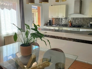 Een moderne keuken met witte kasten, een glazen eettafel en een plant in een pot.