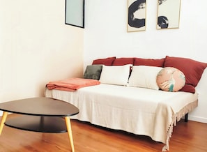 Een kamer met een bank, een ronde tafel en een witte muur met twee ingekaderde kunstwerken.