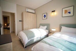 A hotel room with two beds, a wardrobe, an air conditioning unit, and a door leading to another room. - Wonderful 3-bedroom apartment with AC in vibrant riyadh (الرياض)