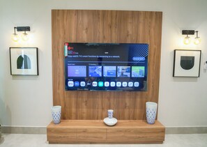 A flat-screen TV mounted on a wooden wall with a framed picture to the left and a wall-mounted light fixture to the right. - Wonderful 3-bedroom apartment with AC in vibrant riyadh (الرياض)
