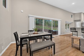 A dining area with a table and chairs, a bench, and a view of a wooded area through large windows. - Escape to Pandapas Retreat! Enjoy a private hot tub, cozy comforts, and peaceful woodland scenery. (Newport)
